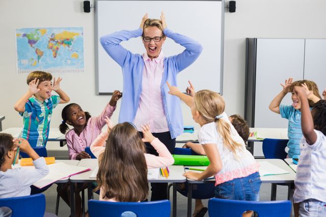 Teacher engaging with a group of energetic students in a classroom. The children are excited and interacting with the teacher, creating a lively and fun learning environment. Ideal for use in educational materials, school brochures, and articles about teaching methods and classroom management.