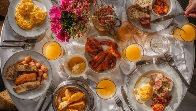 Serving colorful brunch spread with bacon, eggs, orange juice and pastries, overhead