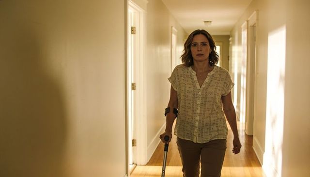 Midlife woman walking with crutch and arm brace in sunlit home hallway showing resilience now