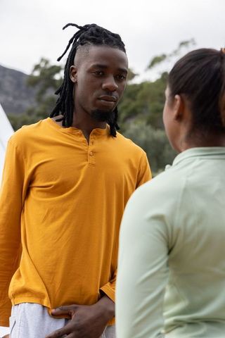 Diverse couple talking at campsite, man wearing mustard henley, outdoor conversation