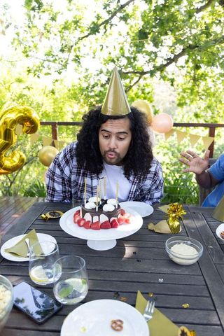 Hispanic male blowing out cake candles in festive birthday celebration