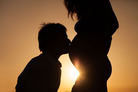Romantic silhouette of man kissing pregnant belly at sunset