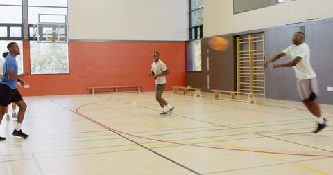 Young men playing basketball in school gym passing and cutting during team practice