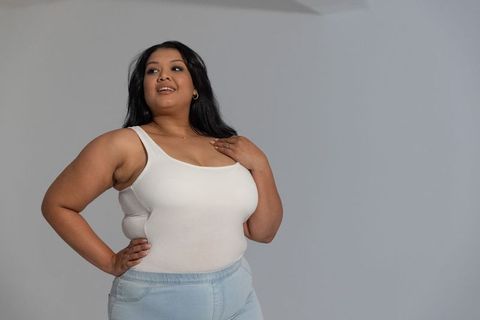 Confident asian woman posing in white tank top and light blue jeans, casual plus-size