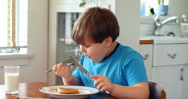Young boy enjoying a breakfast of pancakes in a cozy kitchen setting. Perfect for use in lifestyle, nutrition, and family-related content.