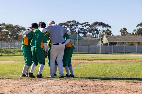 Coach leading youth baseball team huddle on field showing unity, strategy, leadership