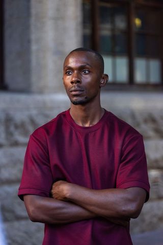 African american man standing outside crossed arms wearing maroon tee contemplating headshot