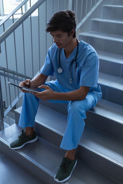 Front view of Caucasian male surgeon using digital tablet on stairs at hospital