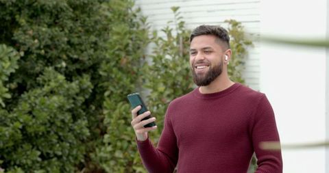 Smiling man with smartphone and earbuds in casual outdoor setting