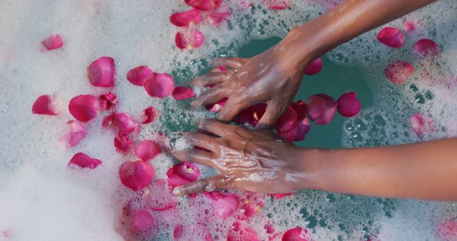 African american woman taking bath and touching flower petals in water in bathroom. health and beauty concept.