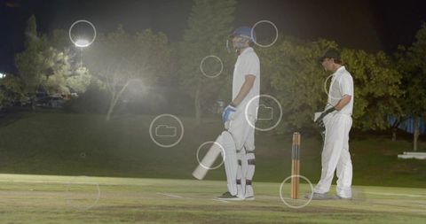 Night cricket match batsman standing at crease under floodlights with wicketkeeper waiting