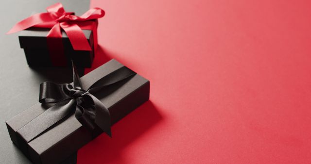 Two black gift boxes with red and black ribbons on black and red background with copy space. Luxury treat, present, shopping, black friday sale and retail concept digitally generated image.