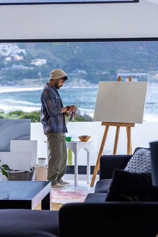 Artist preparing brushes beside blank canvas in coastal studio with ocean view