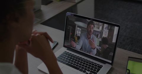 Woman watching colleague speaking during remote video meeting on laptop in coworking office