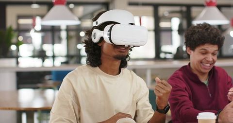 African American men testing VR headset in coworking cafe, laughing and collaborating