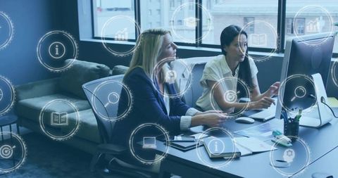 Female Colleagues Analyzing Data on Desktop with Digital UI Icons Overlay in Office