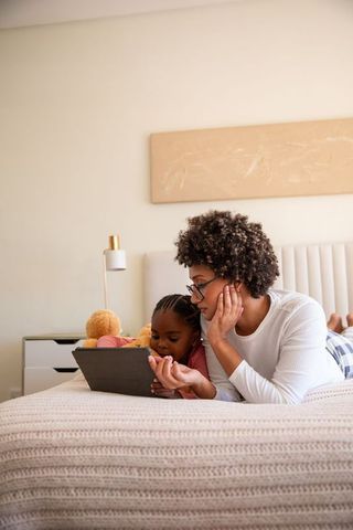 Mother and daughter bonding while watching tablet on bed