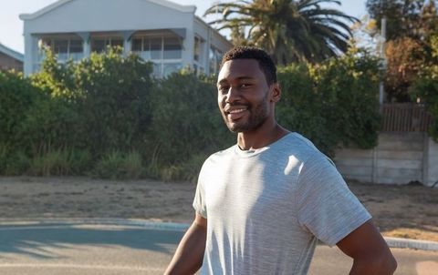Confident african-american man standing outdoors smiling in gray athletic shirt near beach house