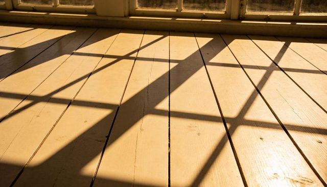 Casting geometric window grid shadows across sunlit painted wooden floorboards
