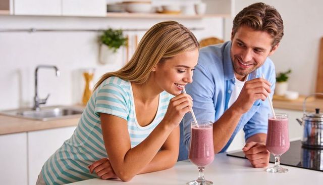 Young couple sipping berry smoothies at bright modern kitchen island, smiling lifestyle