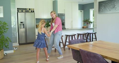 Joyful mother and daughter dancing together in bright modern open-plan kitchen