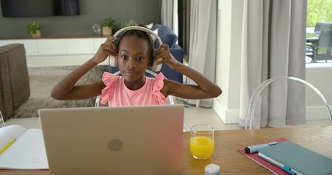Young african girl adjusting headphones while studying on laptop for remote learning