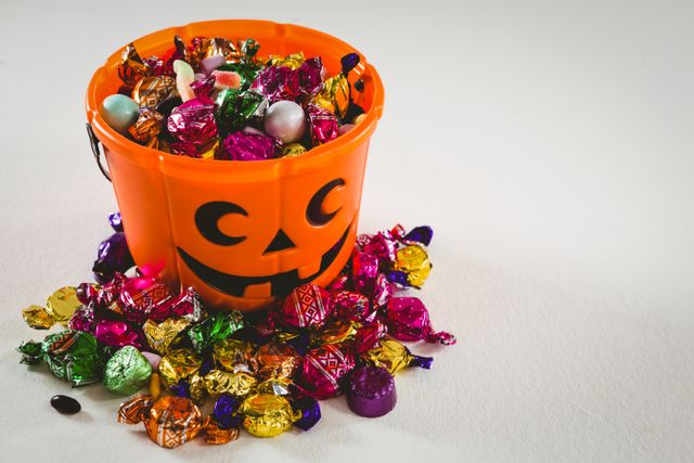 Brightly colored candies spilling out of an orange pumpkin bucket, perfect for Halloween-themed promotions, party invitations, festive decorations, or holiday marketing materials.