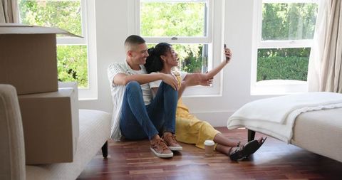 Happy couple taking selfie during moving day in new home