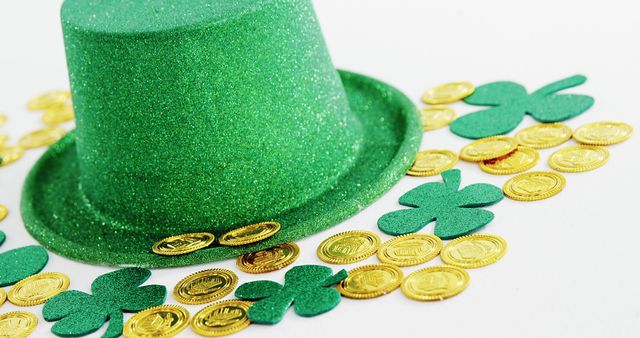 A green glittery hat is surrounded by gold coins and green shamrocks, symbolizing celebration and luck, with copy space. These items are often associated with St. Patrick's Day festivities and Irish culture.