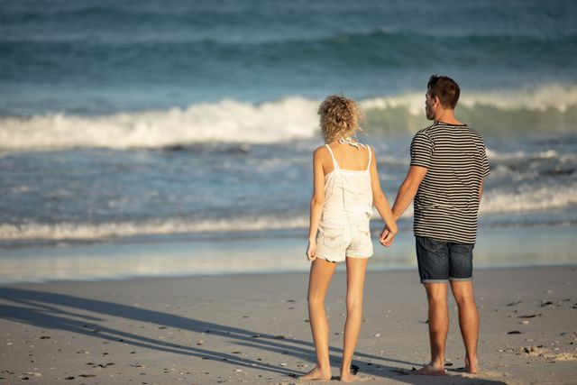 Rear view of couple standing together hand in hand on the beach