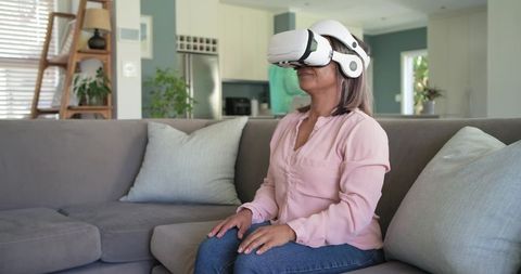 Mature woman experiencing virtual reality on couch at home, modern senior VR lifestyle