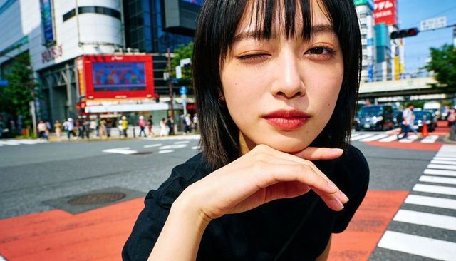 Young woman winking and resting chin at red crosswalk in bustling urban street