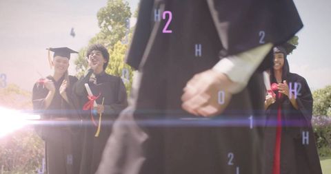 Sunlit graduates celebrating on lawn with walking graduate holding diploma and mortarboard