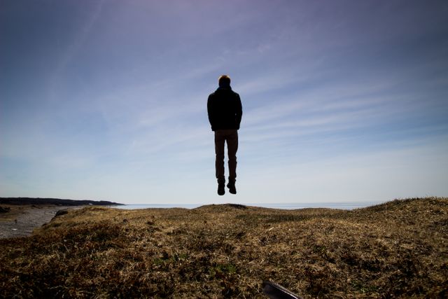 Person appears to be levitating over a rocky landscape under a clear blue sky. The composition exudes a sense of mystery and surrealism, perfect for concepts of magic, unique experiences, and the beauty of nature. This can be used in projects focusing on the supernatural, fantasy, and outdoor adventures.