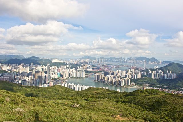 Vibrant panoramic view of Hong Kong's skyline, juxtaposing lush green hills with urban skyscrapers. Ideal for travel blogs, tourism brochures, urban planning presentations, real estate advertising, and nature versus urbanity discussions.
