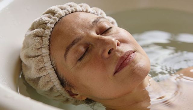 Middle-aged woman soaking in bathtub wearing terry shower cap relaxing serene spa moment