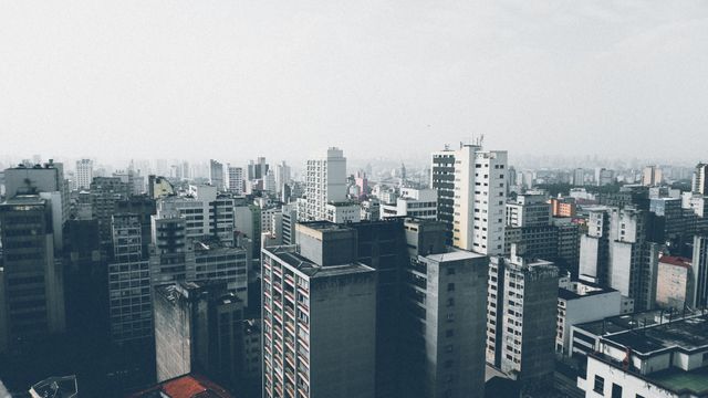Image captures a cityscape featuring a multitude of high-rise buildings under a grey, hazy sky. The scene portrays an urban environment densely packed with diverse architectural structures. Ideal for urban planning presentations, backgrounds for city-themed projects, or materials depicting metropolitan life and urbanization effects.