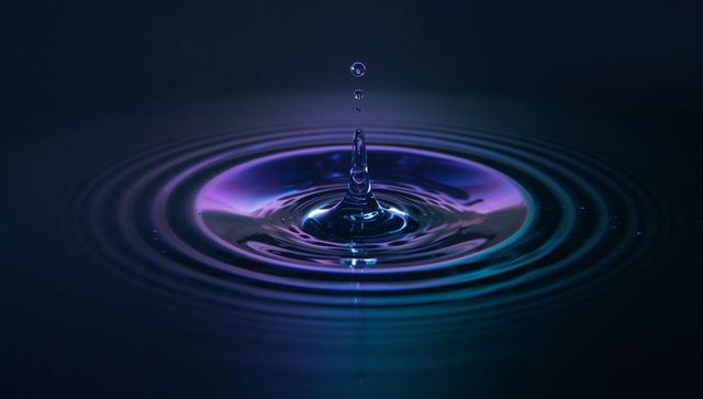 Water droplet splash with purple blue ripples in studio lighting