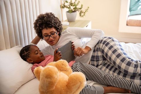 Mother and Daughter Relaxing in Bed Using Tablet for Fun Screen Time