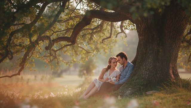 Romantic Couple Relaxing Under Majestic Oak Tree in Tranquil Meadow
