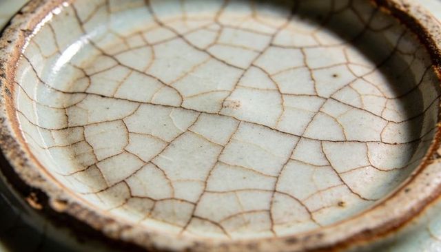 Displaying crackled glaze on antique ceramic dish with worn brown rim and patina