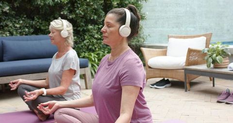 Mature women practicing guided meditation outdoors with headphones on yoga mats
