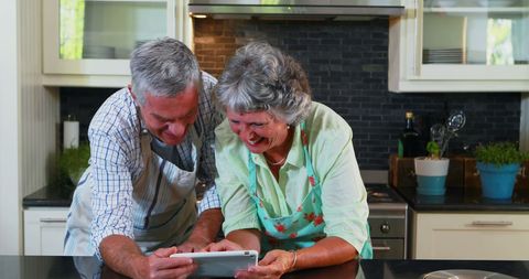 Senior Couple Using Tablet in Modern Kitchen, Laughing Together