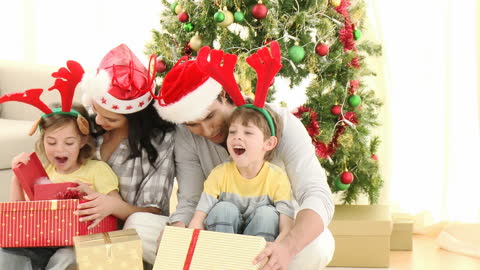 Happy Family Unwrapping Christmas Gifts by Decorated Tree
