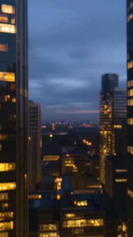 Vertical dusk skyline revealing city towers lighting up from office window during twilight