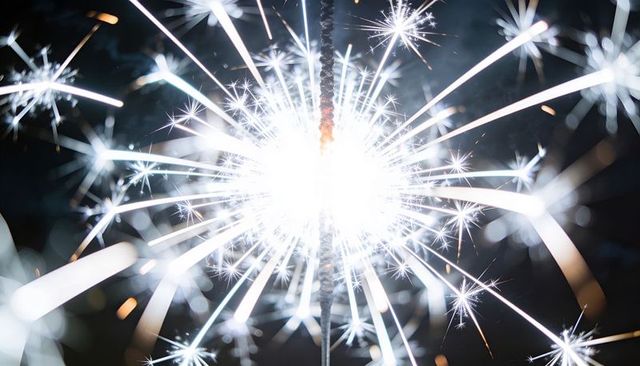 Handheld sparkler emitting intense white sparks and radiant trails on dark background