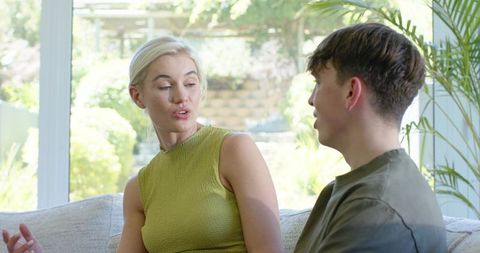 Mother and teen son discussing on sofa in bright living room, casual family conversation
