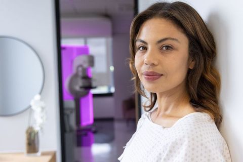 African american woman standing in modern clinic wearing exam gown, calm confident patient