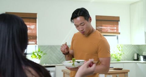 Asian couple tasting meal with chopsticks at bright modern kitchen island