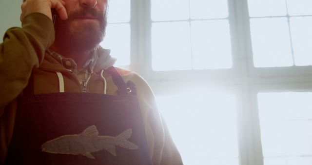 Man wearing apron with fish emblem talking on phone in sunlight - Download Free Stock Images Pikwizard.com